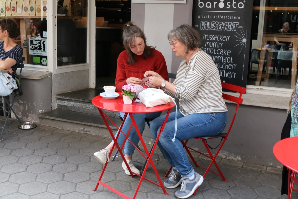 Two women sitting at a table of a café in the pedestrian zone and looking at a knitting project in concentration